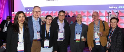 A group of people posing with name badges in front of the primary stage at ISHLT2023 in Denver