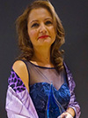 Woman with light brown hair posing in a blue velvet and sheer top and purple shaw