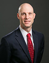 Bald man wearing white button down, red tie, and black suit jacket
