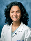 Woman with black curly hair wearing a white doctor's coat smiling
