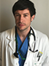 White man with brown hair wearing blue scrubs and a white doctor's coat