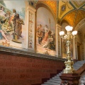 Photo of a museum staircase with large paintings on the wall
