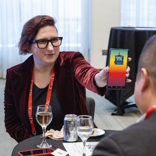 woman showing phone screen with ISHLT2026 app splash screen