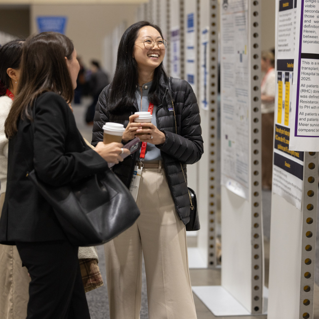 An Asian woman with long, black hair and round glasses laughs with attendees at the ISHLT2026 poster hall