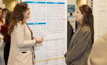 Two white women with long, light brown hair talk in front of a scientific poster
