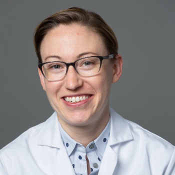 A headshot of Lauren Truby wearing glasses and a white lab coat against a grey background