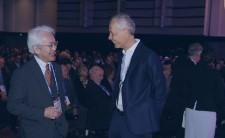 Two men talking and smiling with a crowd of people behind them