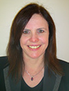 White woman with dark brown reddish hair, wear a blue jeweled necklace smiling